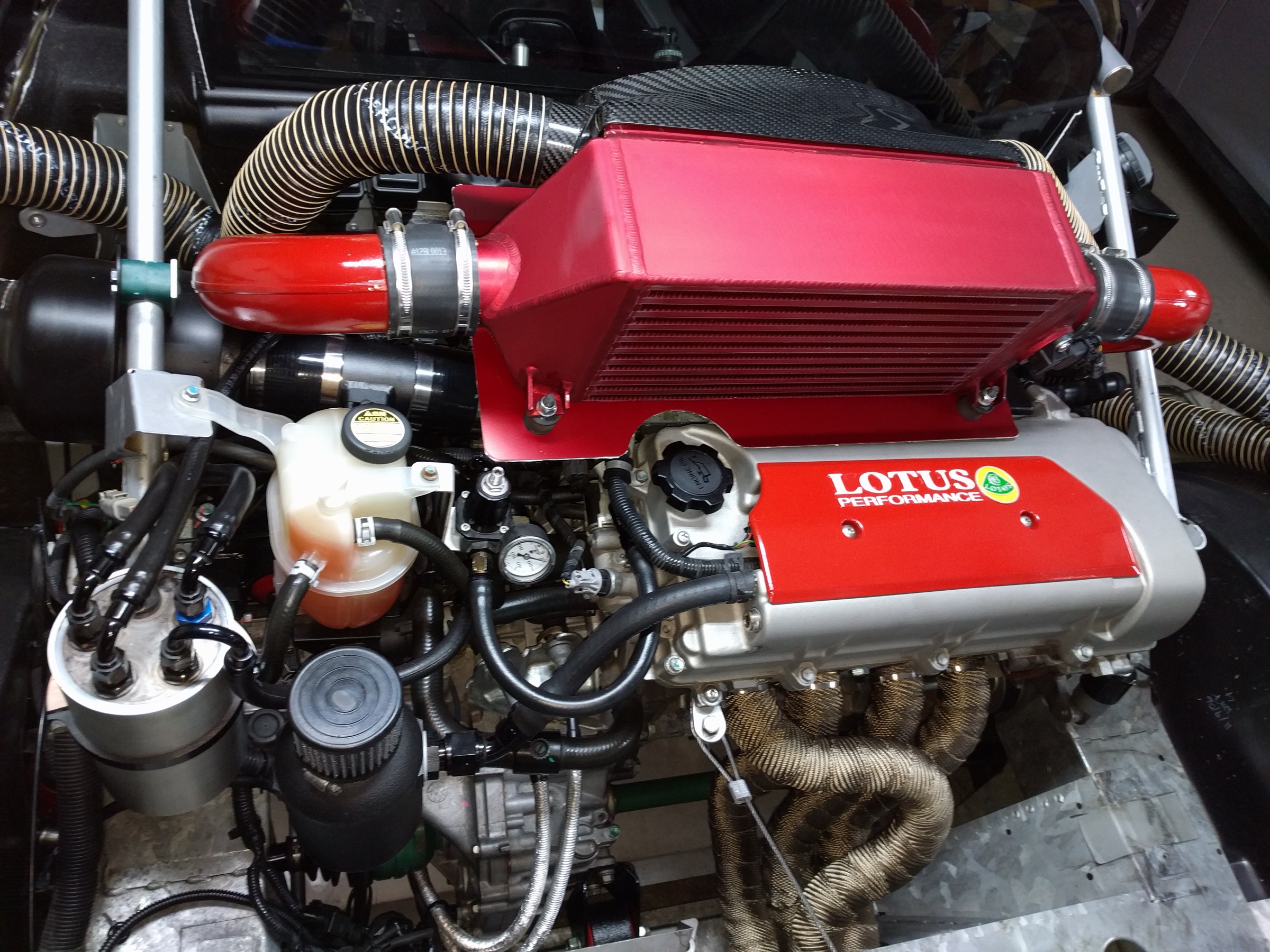 Lotus 2ZZ-GE engine bay with red RLS intercooler, intake plumbing and silver fuel surge tank