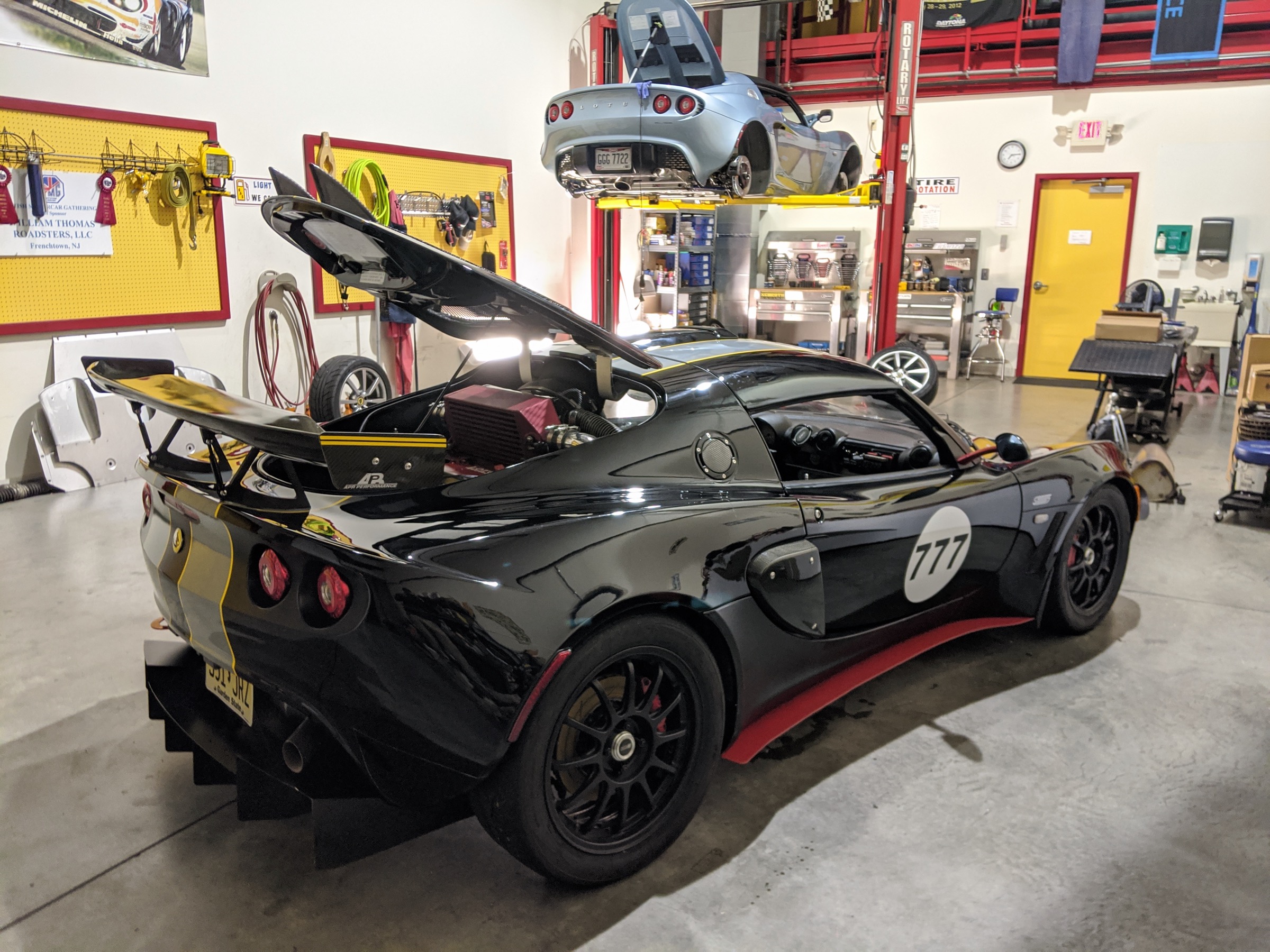 Black Lotus Exige number 777, rear three-quarter view in a workshop with the engine cover open