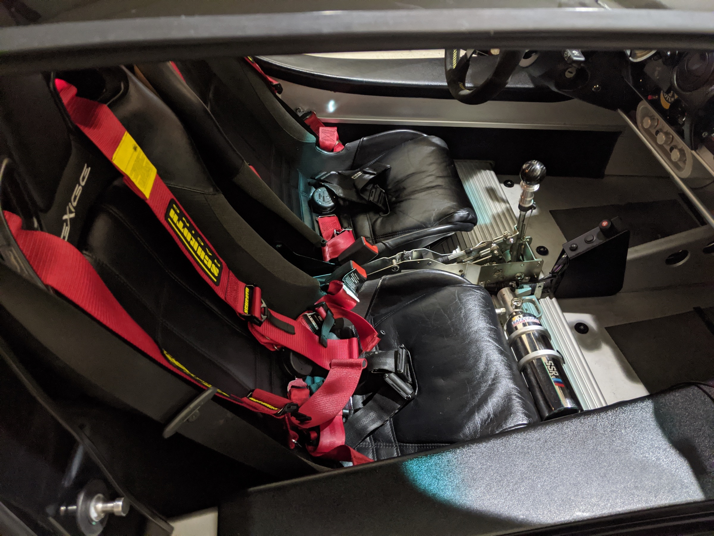 Lotus Exige cockpit showing the LETSLA shifter mechanism, racing seats and red harnesses