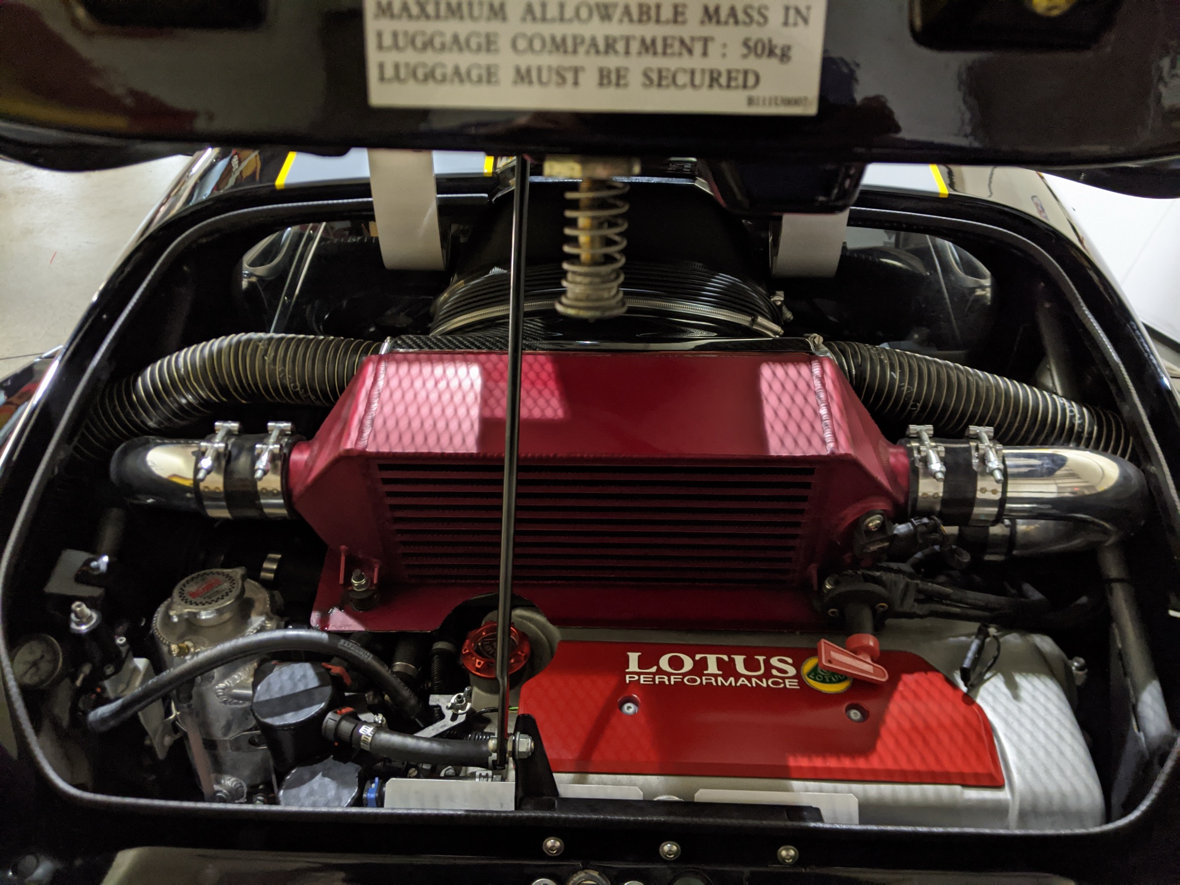 Lotus engine bay after the cooling overhaul — RLS intercooler, Lotus Performance cam cover, and the BOE pressurized swirl header tank with red cap visible at left